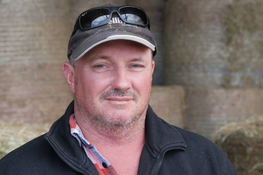 A man in a cap and sunglasses stands in a hay shed.