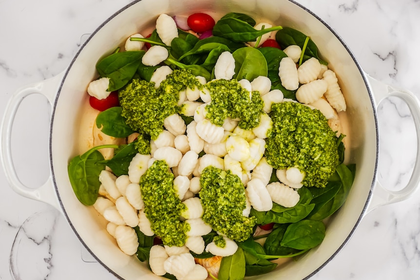 Ingredients including uncoooked gnocchi and pesto sit together, unmixed, in pot.
