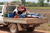 An injured man lies on back of a ute with two people caring for him