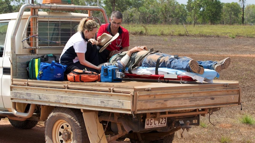 An injured man lies on back of a ute with two people caring for him