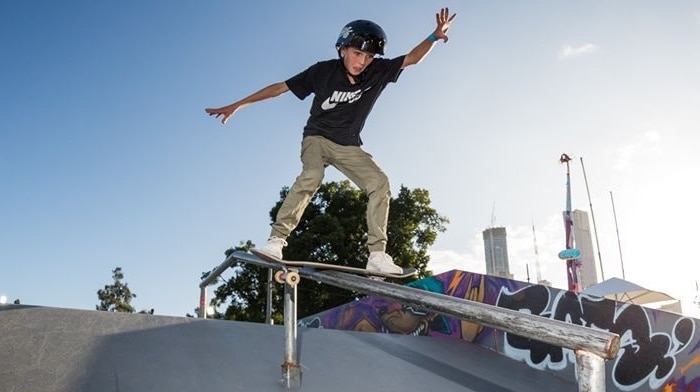 A child skates off a pole on a sunny blue sky day, wearing long khaki pants, black t shirt and helmet