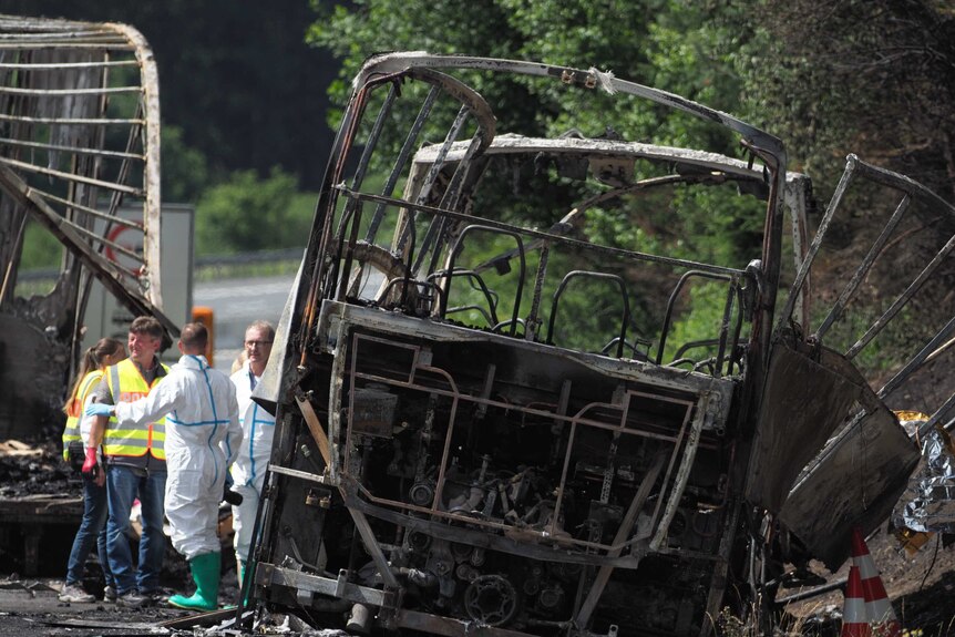 The burnt-out frame of a bus sits on the side of a motorway.