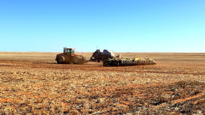 A tractor pulls a disk seeder in a dry field
