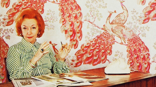 A woman with red hair sits in an office with brightly coloured wallpaper behind her