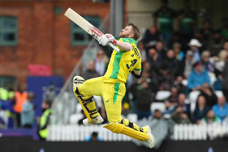 David Warner leaps high in the air, preparing to push his right arm, which is carrying his helmet, further into the air.