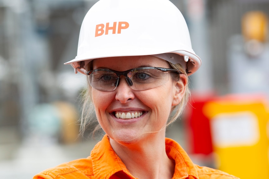 A woman wearing a hi-vis orange shirt and a white hard hat stands with her arms folded