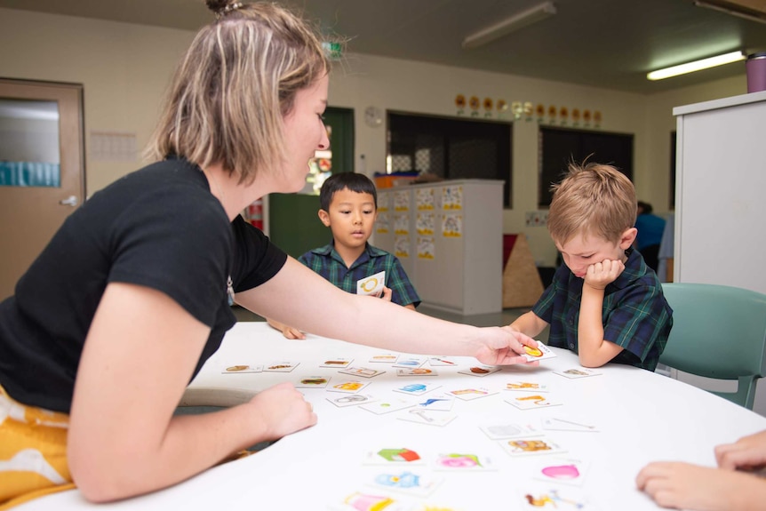 Two young male students are helped in an activity by a female teacher.