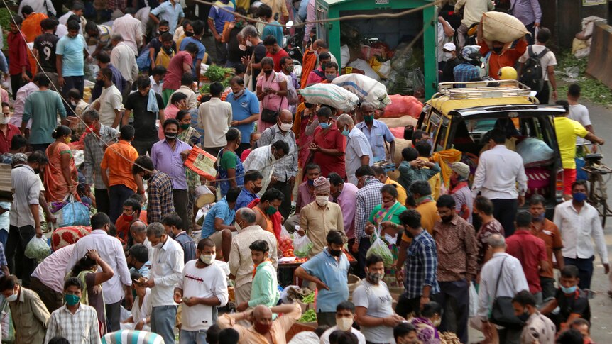 Dozens of people crowd a busy marketplace in India. Some people are wearing face masks.
