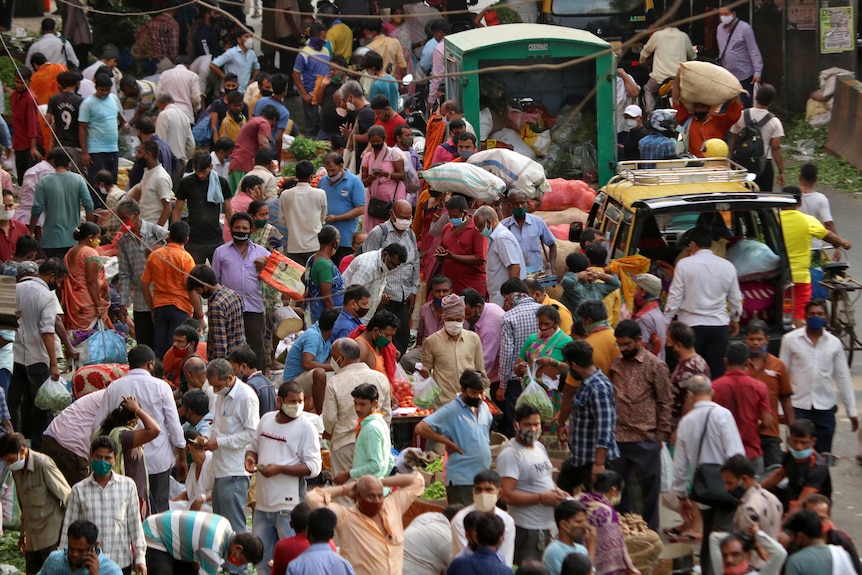 Dziesiątki ludzi gromadzą się na zatłoczonym rynku w Indiach.  Niektórzy ludzie noszą maski na twarz.