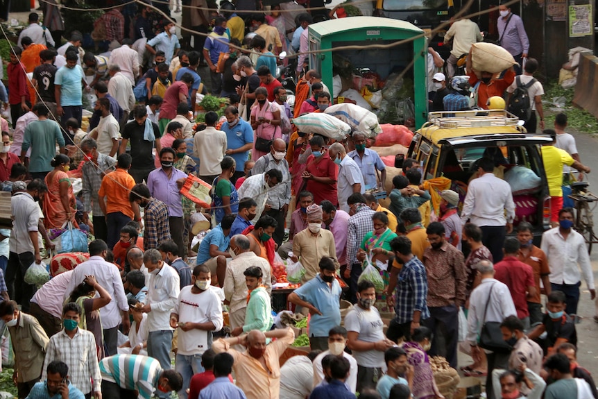 Dozens of people crowd a busy marketplace in India. Some people are wearing face masks.