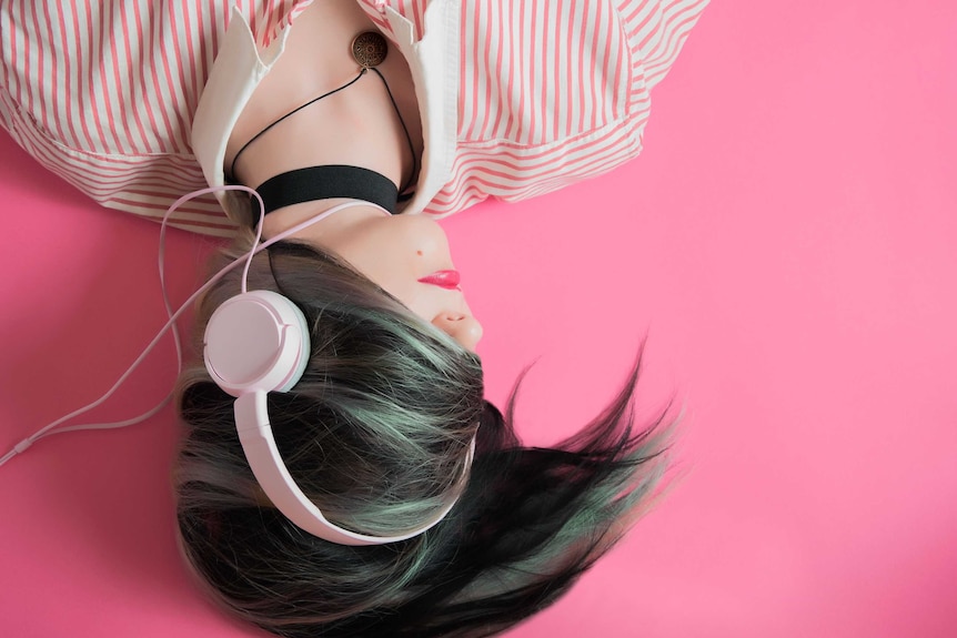 Girl wearing headphones lies on pink floor