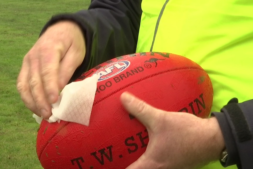 Someone in high-vis wiping down a football with a sanitary wipe.