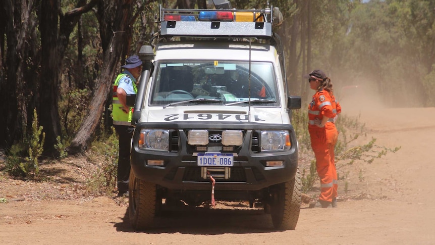 A police officer and a SES volunteer stand either side of a police vehicle in the bush during the search.