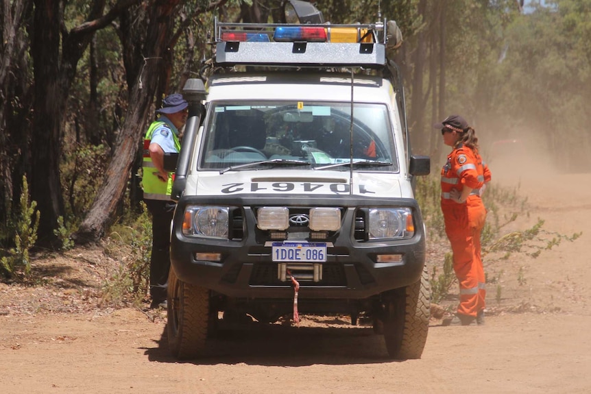 A police officer and a SES volunteer stand either side of a police vehicle in the bush during the search.