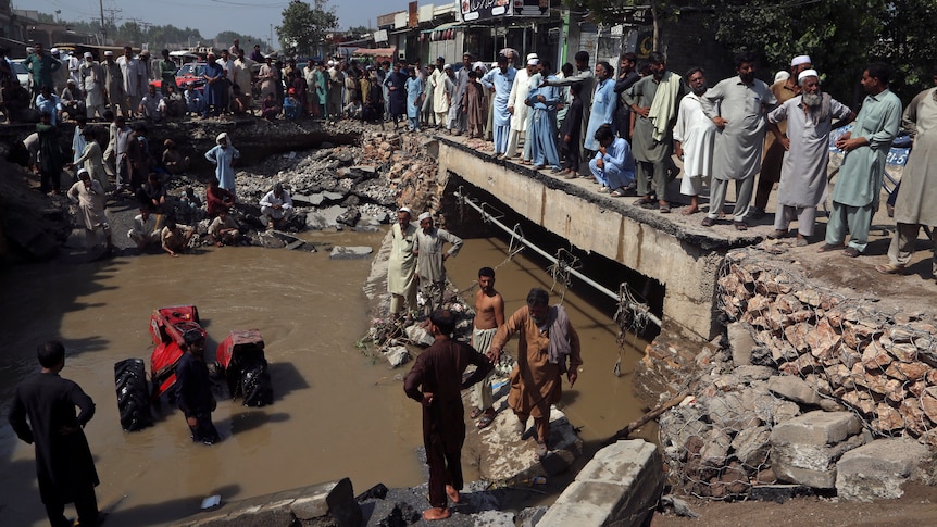 A crowd of people surround a washed-out road