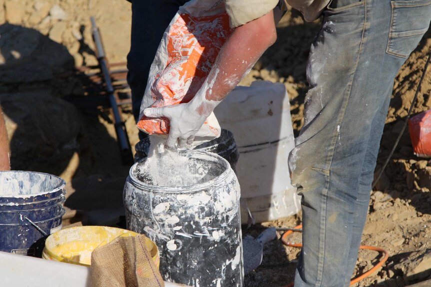 A man mixing plaster in a black plastic bucket.