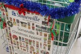 A sign soliciting food donations for a charity appeal, attached to a trolley decorated with tinsel.