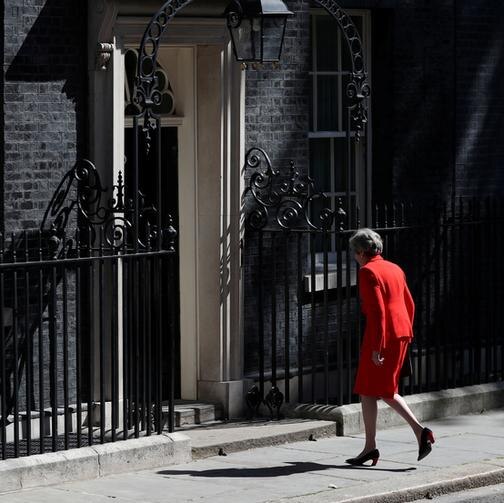 Theresa May wears a red suit and walks with her back to the camera back to the black 10 Downing Street door.