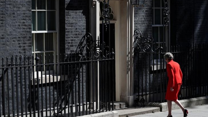 Theresa May wears a red suit and walks with her back to the camera back to the black 10 Downing Street door.