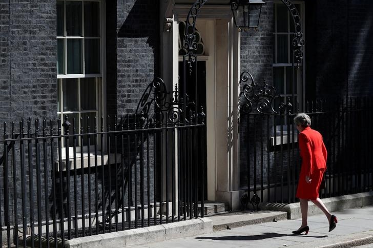 Theresa May wears a red suit and walks with her back to the camera back to the black 10 Downing Street door.