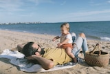 Man and his toddler daughter sitting on him while on the beach for a story about where new dads can find support.