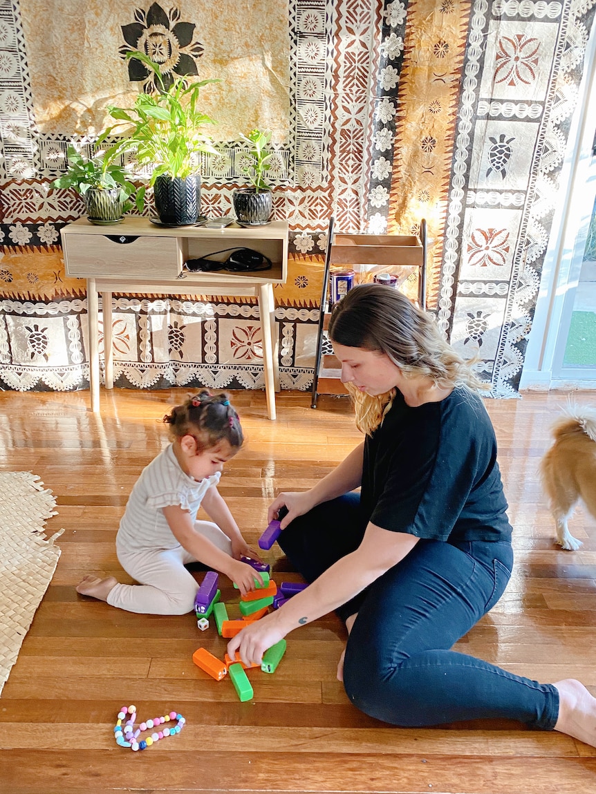A little girl and her mother play with kids blocks on a shiny wooden floor