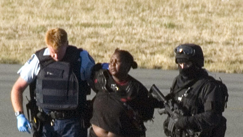 A woman is escorted by New Zealand police across the tarmac at Christchurch airport 8 February, 2008