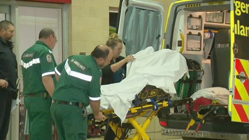 Paramedics move a stretcher into an ambulance.
