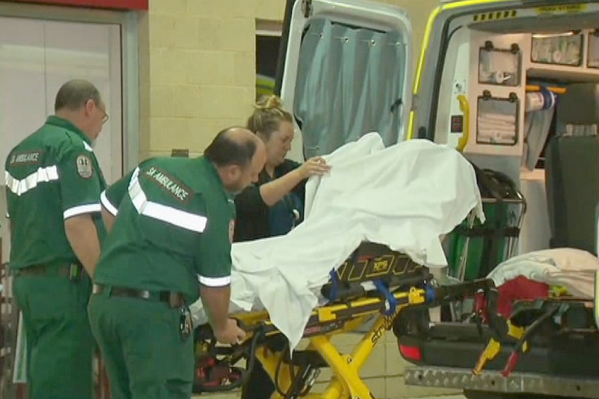 Paramedics move a stretcher into an ambulance.