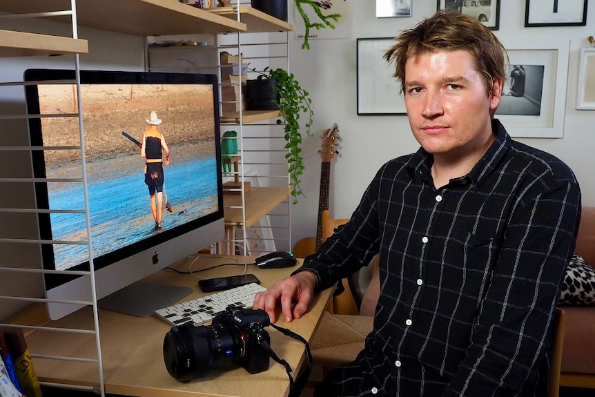 Jason sits in in front of a computer screen with his camera on the table in front of him.