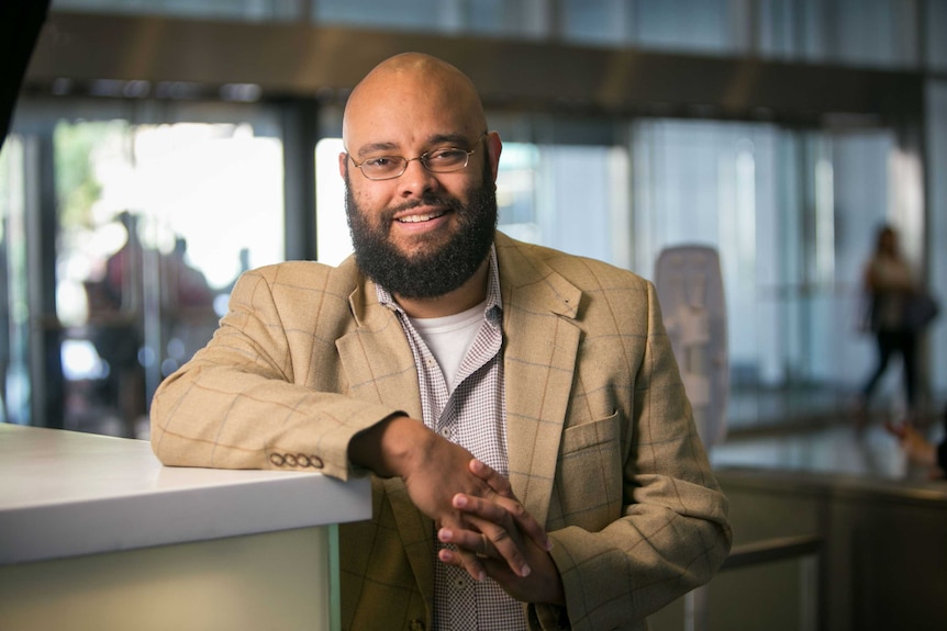 Dr Goff, he is wearing a beige suit and smiling in an office, he's a black man with a beard and glasses.