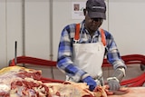 a man in a hat and apron cutting up a carcass.