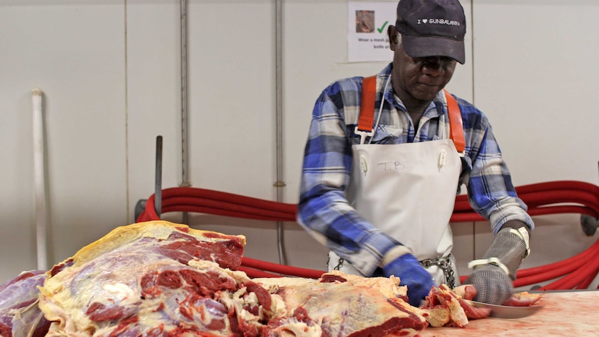 a man in a hat and apron cutting up a carcass.