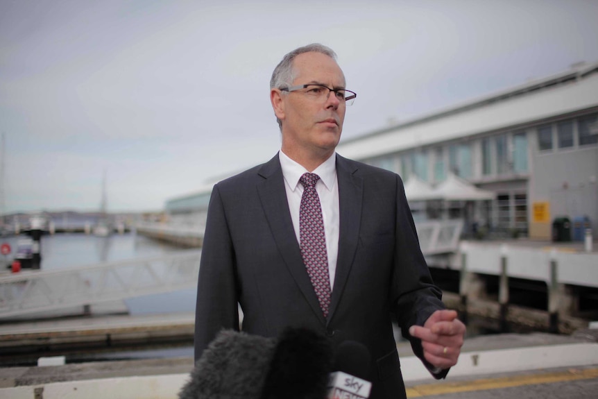 A man in a suit stands in the foreground of a ferry terminal