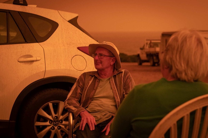 A man sits in a chair near the ocean in a red haze