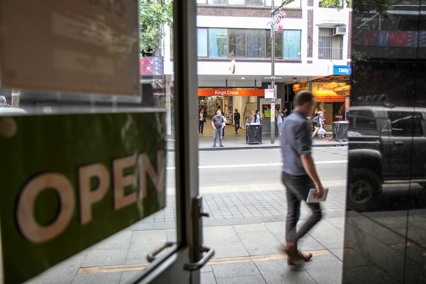 A photo looking outwards from a safe injecting room as a man walks past, with a sign that reads 'kings cross' in the distance.