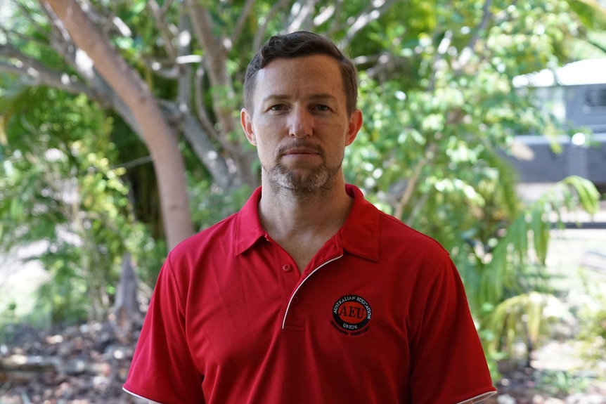 Man wearing a red polo shirt with an Australian Education Union logo posing for camera mugshot