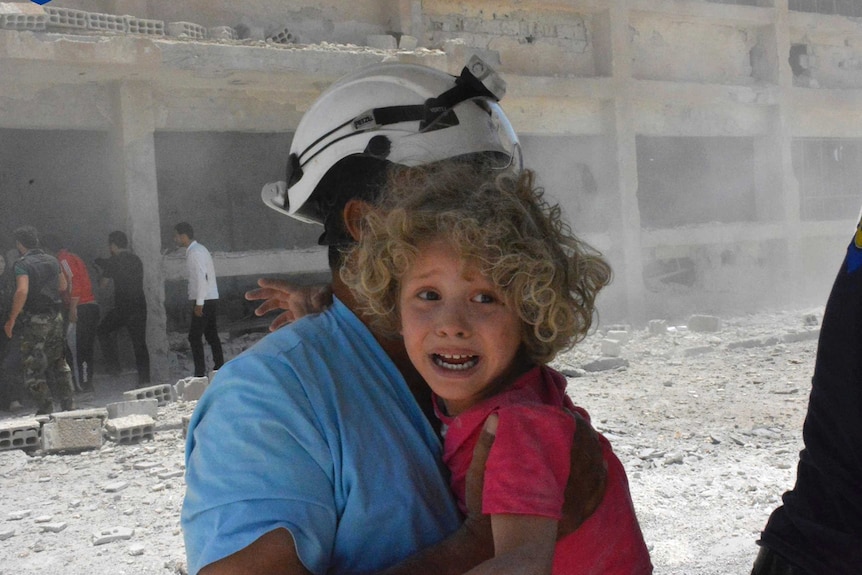 A civil defence worker carrying a child after airstrikes hit a school
