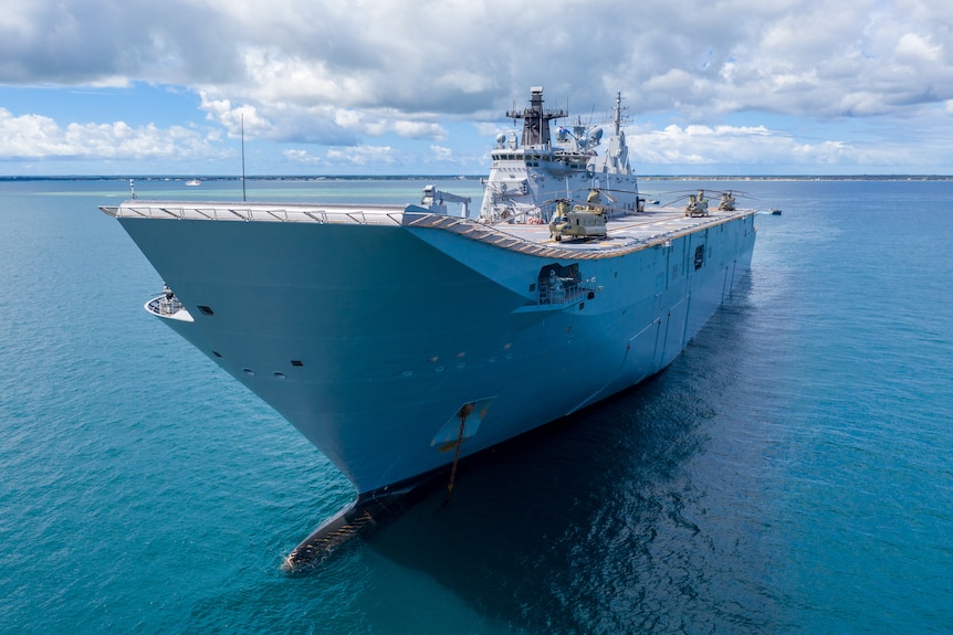 A closeup of HMAS Adelaide warship in the ocean on a sunny day, with clouds in the sky above it