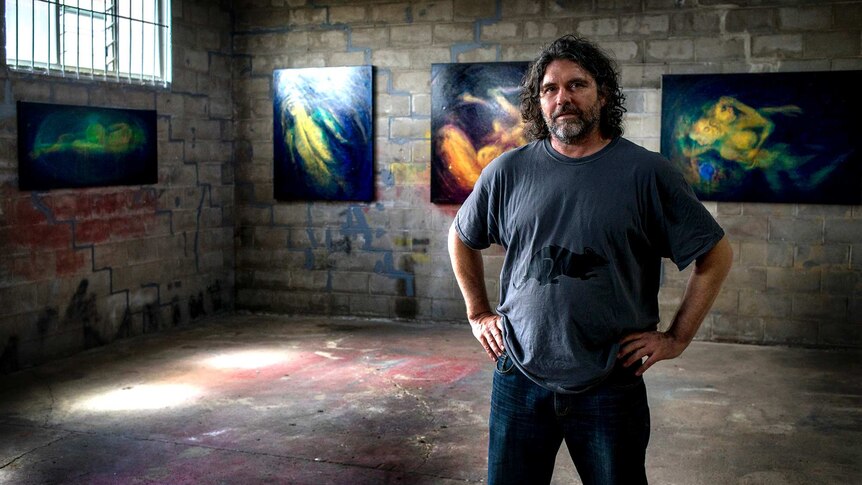 Man stands in industrial art space with oil paintings.