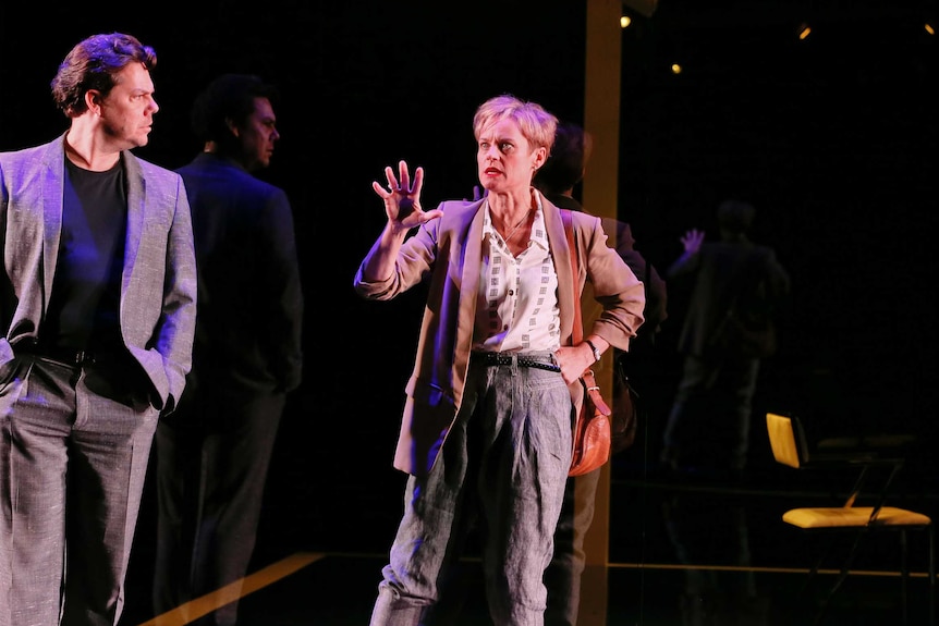 Jason Klarwein (left) and Nadine Garner (right) in front of a glass window on a black stage.