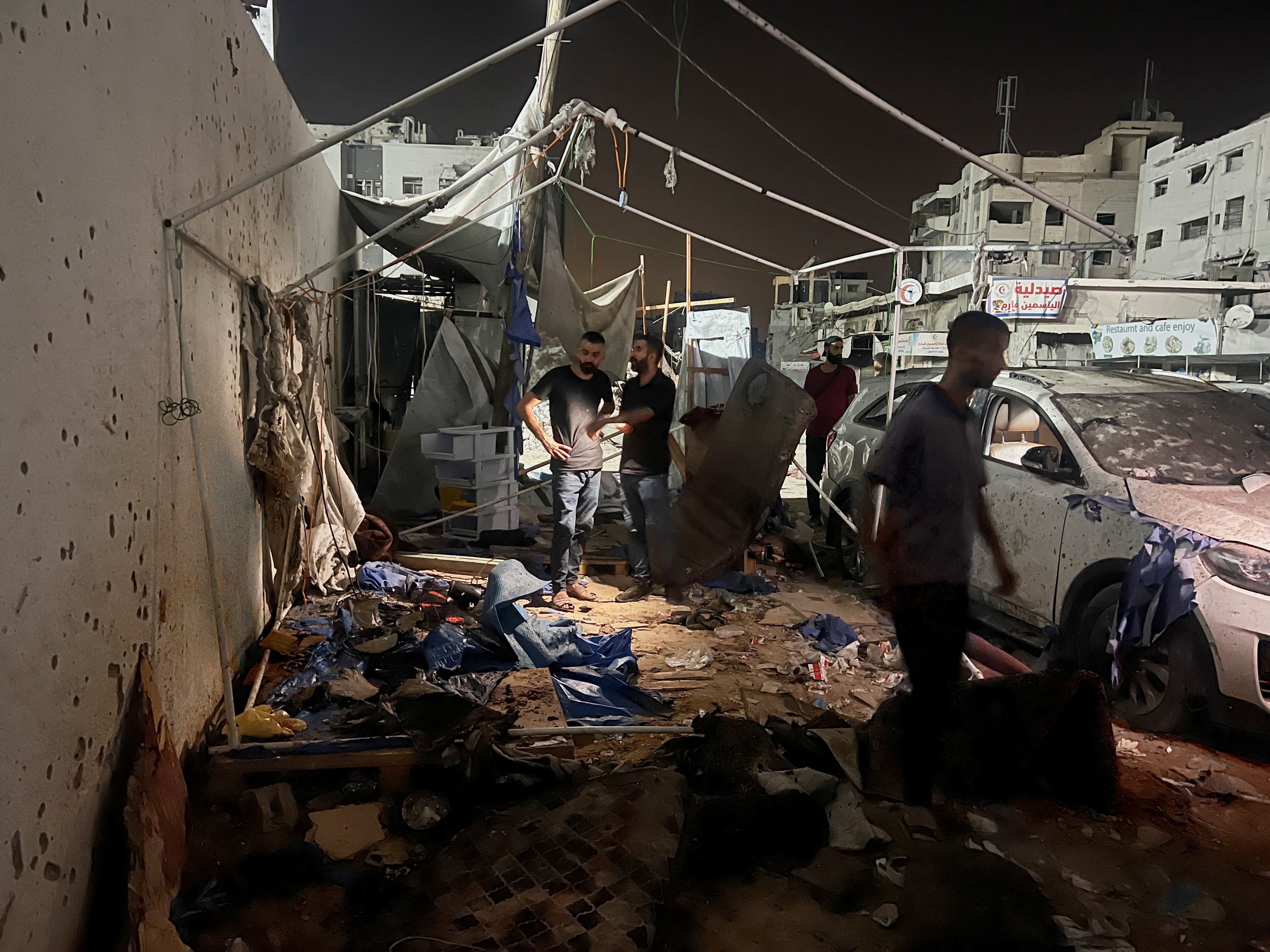 People look at the burnt and tattered remains of a tent on a street.