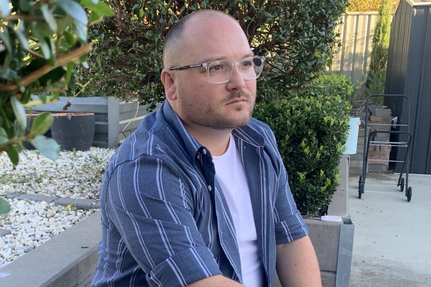 A man sits in a garden and looks to the side of the camera.