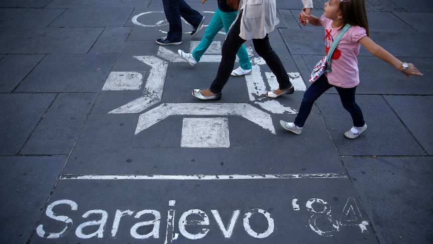 People walk past logo of Winter Olympics painted on street in central Sarajevo