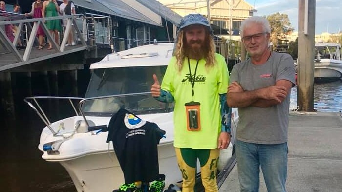 Man with beard and paddle board gives thumbs up alongside another man at wharf