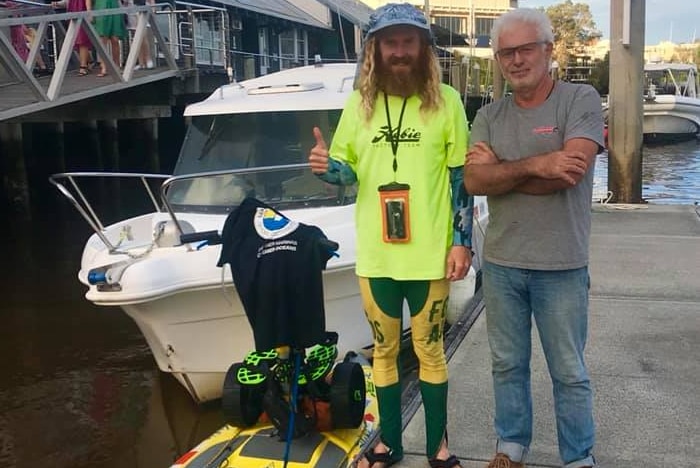 Man with beard and paddle board gives thumbs up alongside another man at wharf