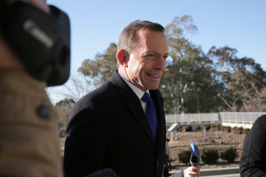 Tony Abbott grins as reporters try to interview him outside Parliament