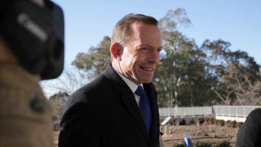 Tony Abbott grins as reporters try to interview him outside Parliament