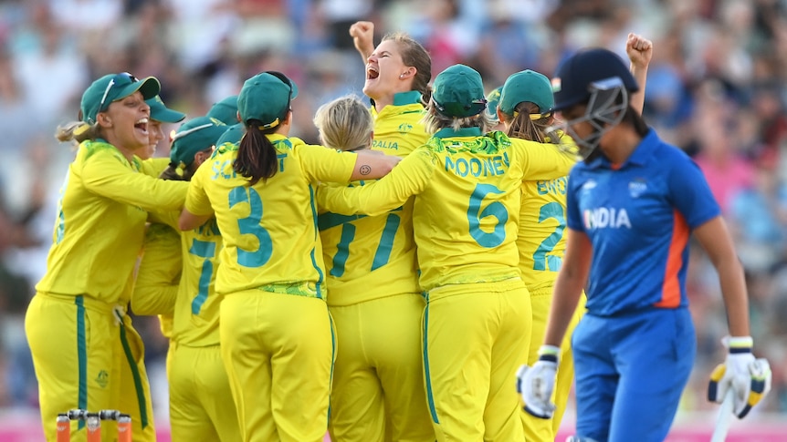 Australia's women's cricket team crowd together to hug and cheer and punch the air after clinching gold.