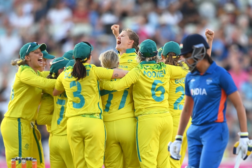 Australia's women's cricket team crowd together to hug and cheer and punch the air after clinching gold.
